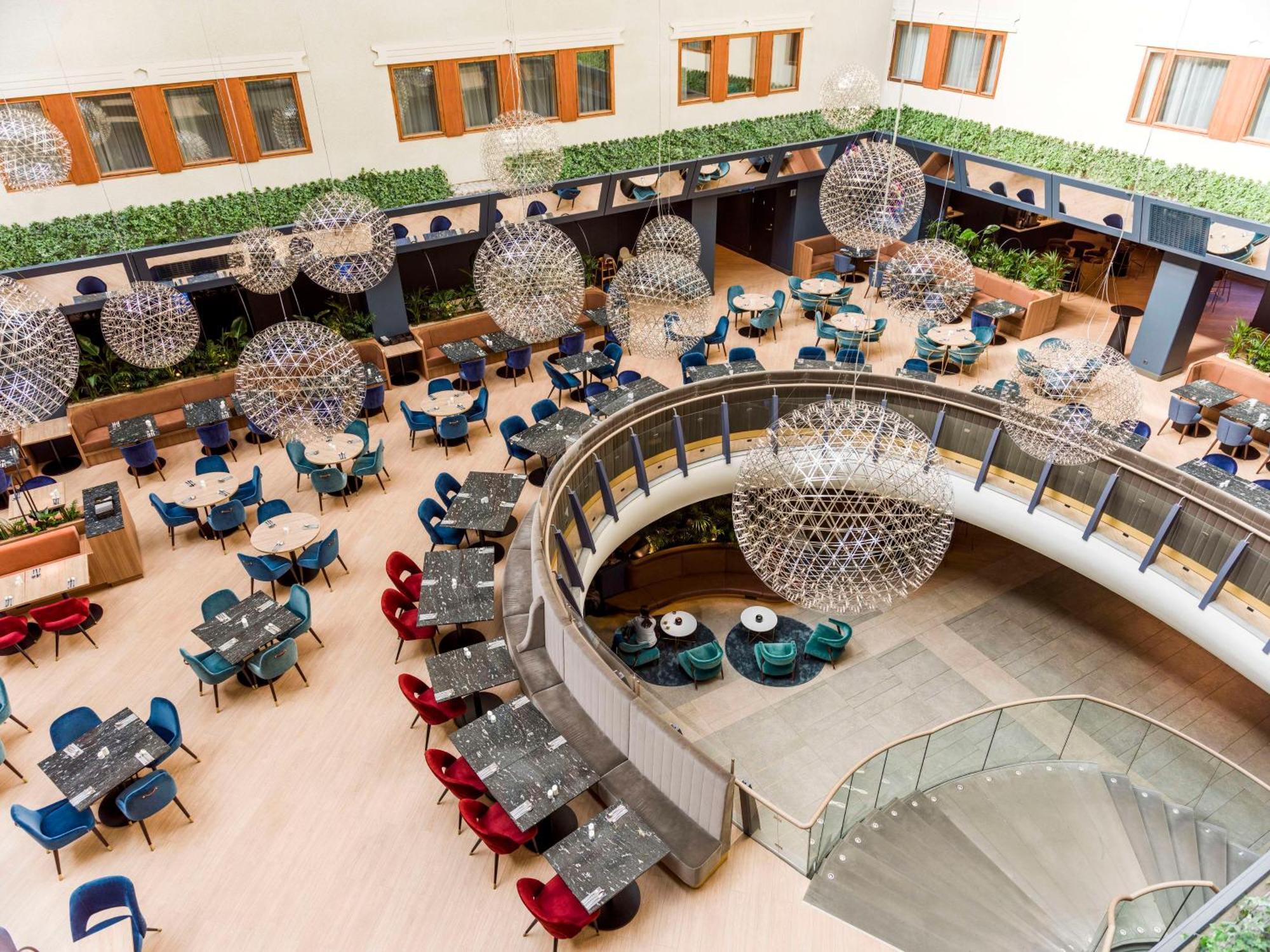 Radisson Blu Royal Viking Hotel, Stockholm Ngoại thất bức ảnh The photo shows a spacious and stylish dining area in a modern restaurant or hotel lobby. It features a variety of round tables arranged in a curved layout, surrounded by colorful chairs in shades of blue, red, and gray. Large, spherical light fixtur